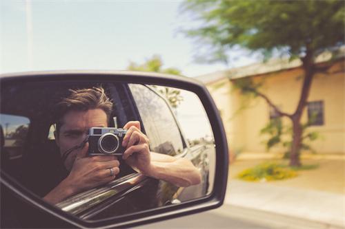 alt="Man with film camera reflected in car mirror"