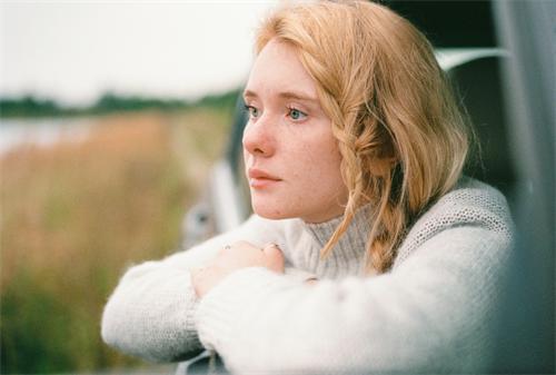 alt="Film-style portrait of a blonde girl in a white sweater by the car"