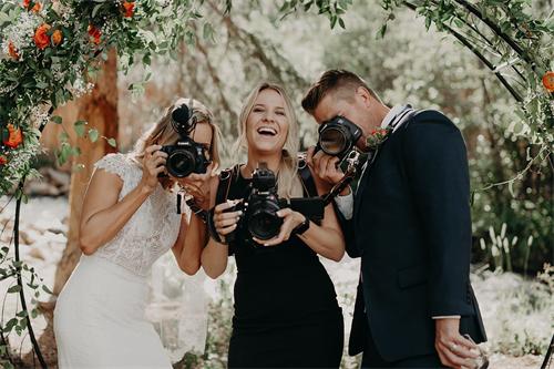 alt="Humorous wedding shot with bride and groom pretending to take photos"