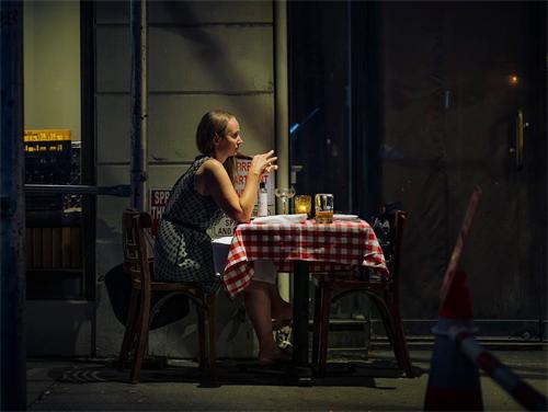 alt="Moody night street photo of a woman at a bistro"